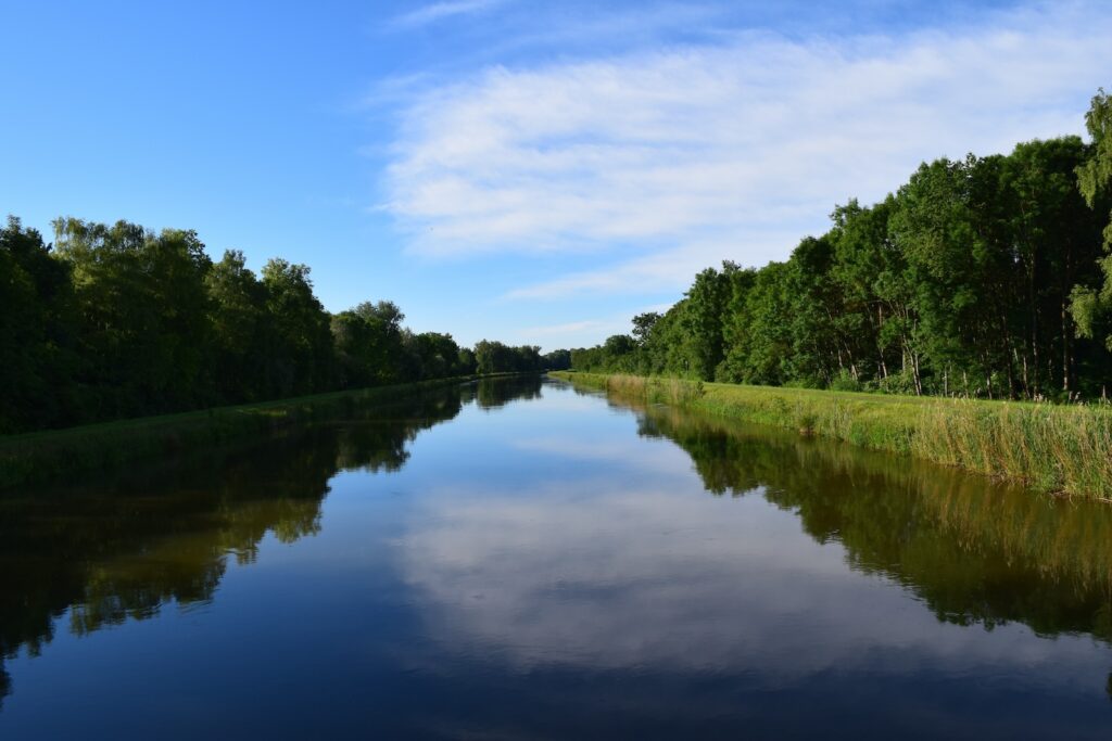 View of slow river with forested and grassy riverbanks.